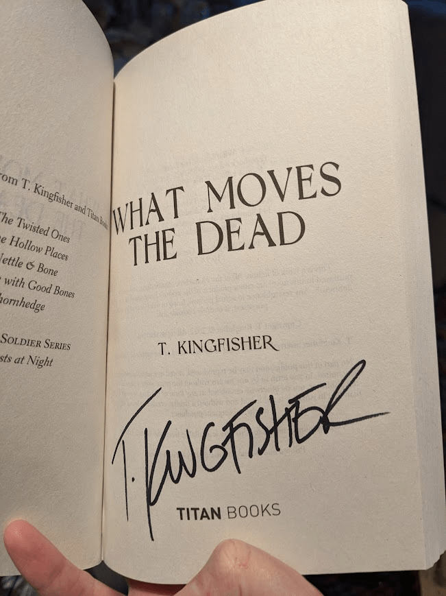 T. Kingfisher's book 'What Moves the Dead' opened to the title page, where the author's signature can be seen. 