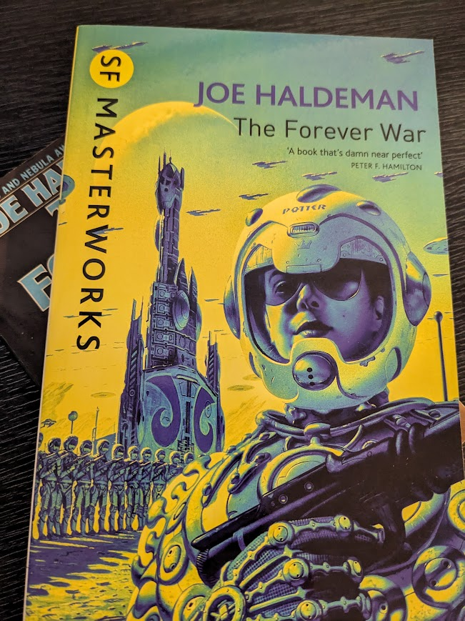Two paperback copies of The Forever War by Joe Haldeman. The bottom copy is barely visible, with only light blue letters on a black background exposed.
The top copy is the SF Masterworks edition, coloured entirely in shades of yellow and blue. A women in elaborate power-armer and a futuristic helmet with the name "Potter" written on it stands to attention in the foreground with a gun held over her chest. Behind her, a row of similarly dressed soldiers stand in line shoulder-to-shoulder in front of a large tower. Spaceships are flying overhead.
Between the title and the woman in the foreground is the following quote by Peter F. Hamilton; "A book that's damn near perfect."